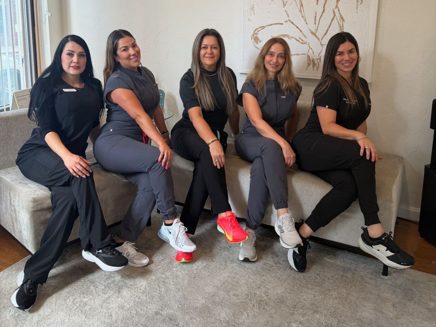 The Boston Cosmetic & Laser Center team, five women in scrubs, smiling together on a sofa in the clinic